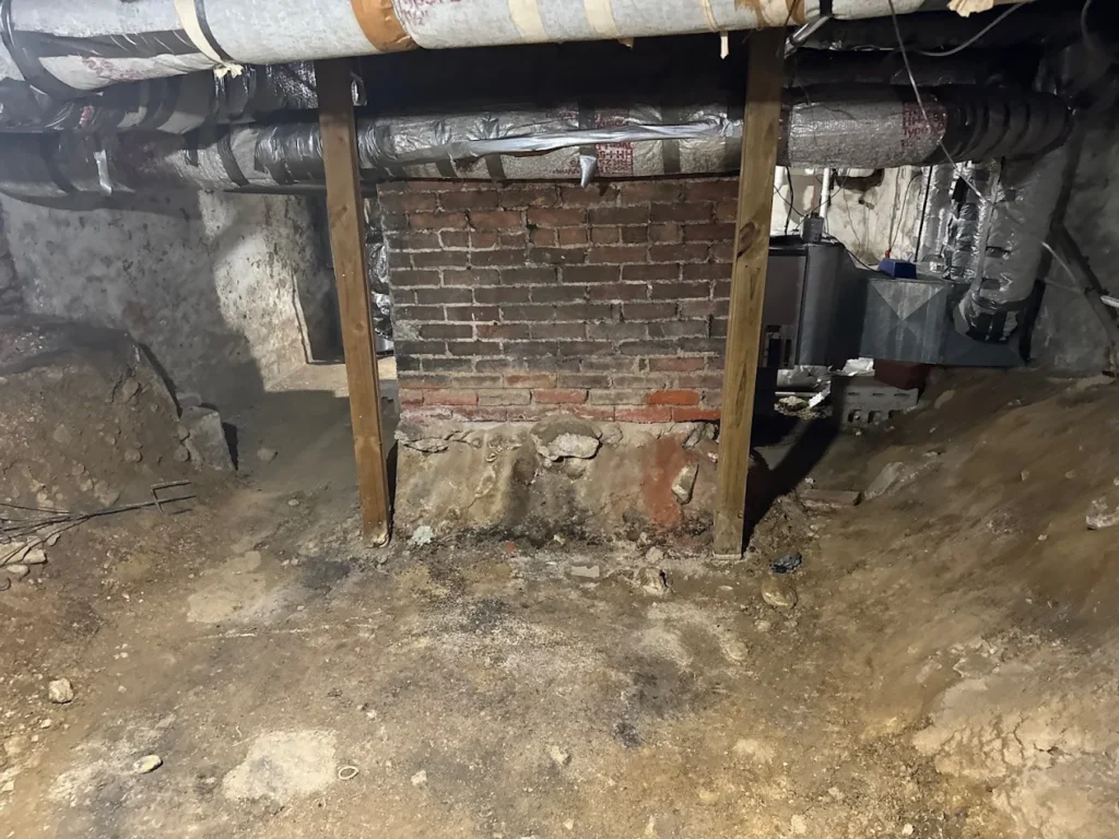 Crawl space with exposed soil and brick foundation showing signs of moisture and potential clay soil pressure damage