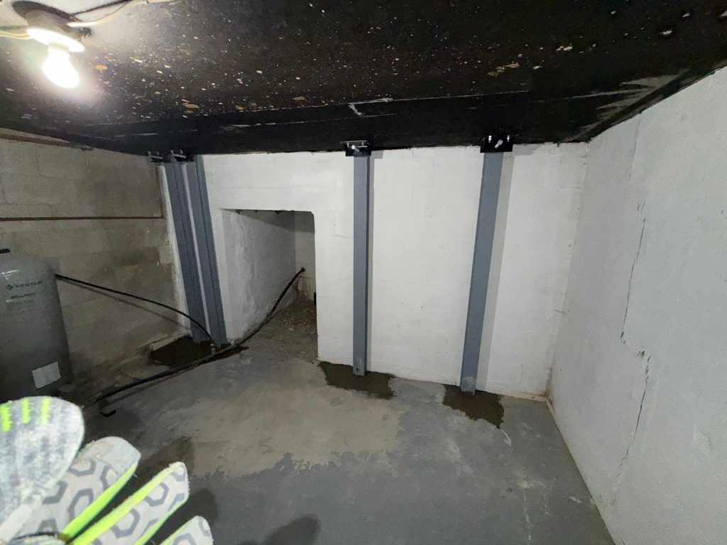 Basement with visible wall cracks, steel support beams, and water seepage caused by freeze-thaw foundation damage